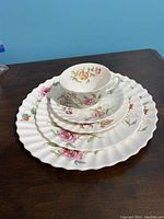 Top down photo of the five-piece place setting showing cup, saucer, two plates and large plate with floral design and scalloped edges.
