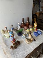 Shows a variety of salt and pepper shakers in animal and decorative shapes arranged on a white paper towel, includes ducks, roosters, birds, bottle shapes, clowns, and fishes.