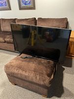 Front view of the Sanyo 41-inch LED TV placed on a brown ottoman, showing screen and bezel with cables.