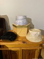 Three vintage women's hats and a hexagonal hat box displayed on a wooden cabinet.