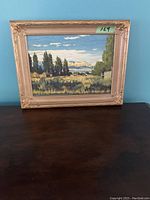 Front view of the framed oil painting on board by Lorne K Smith, showing the landscape scene with trees, meadow, and mountains against a blue sky.
