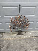 Photo of metal tree of life wall art showing its full structure and painted leaves, placed against a garage door for size reference.
