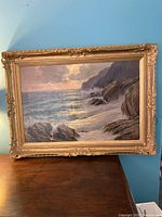 Photo of oil painting on canvas depicting a seascape with rocky cliffs and waves in a gold ornate frame