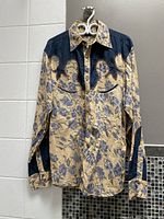 Front view of men's western shirt showcasing floral beige and blue pattern with embroidered dark blue yoke and elbow patches, button-down and collar details.