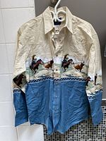 Front view of Wrangler men's western shirt featuring cream and blue fabric with a rodeo print design.