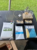 Overview of brand new household items on table including mattress protector, wire baskets, string lights, glass containers, plastic cups, resealable bags