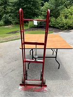 Full front view of red hand truck dolly showing metal frame, wheels, and flat loading base.