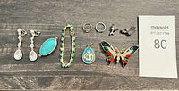 Full view of all jewelry pieces spread on dark surface showing earrings, rings, pendants, bracelet, and brooch