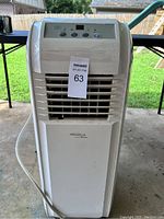Front view of the white portable air conditioner standing on concrete patio showing upper control panel, lower louvers, and side exhaust hose