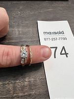 Photo of two gold-tone rings on finger with clear stones, showing front view.