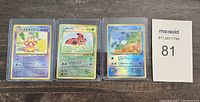 Three 1996 Japanese Pokémon holo foil cards in protective sleeves on a surface alongside a MaxSold card. Cards include Slowpoke, Ledyba, and Marill.