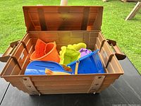 Brown plastic container open showing assorted colorful beach toys including molds and buckets inside.