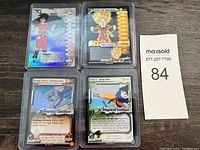 Four vintage Dragonball Z holographic trading cards displayed on a wooden surface, each in plastic protective sleeves.