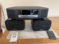 Bose Wave radio with front digital display and CD slot, placed atop two Bose Signature Series speakers, alongside a black Bose remote control.
