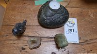 Overview of four carved stone decor pieces including a raccoon, walrus candle holder, and two smaller carvings on a wooden surface with lot card.