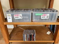 Two Sterilite plastic containers filled with various music CDs on a wooden shelf