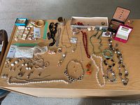 Wide view of costume jewelry laid out on a wooden surface showing necklaces, bracelets, earrings, and jewelry boxes with a taped off adjacent corner.