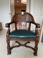 Front view of chair showing cane back, green upholstered seat and carved wooden frame