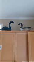 Wide shot image showing the two wooden waterfowl decoys on top of a cabinet, a blue goose on the left and a Canada goose on the right.