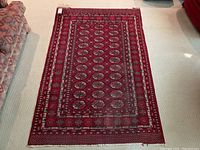 Full view of hand pulled deep red rug with intricate geometric patterns on light carpeted floor.