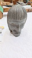 Front angle of carved stone head showing detailed facial features and hair texture.