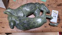 Top view of green carved stone sculpture with two animals intertwined and a broken flipper piece separated to the side.