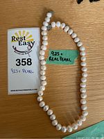 Necklace laid out flat with a Rest Easy auction tag and handwritten label noting '925 + Real Pearl'.