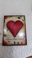 Front view showing rectangular Sid Dickens tile, featuring a prominent raised red heart and floral background design with "Children's Heart Network" text.