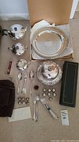 Image showing assorted silver plated serving pieces including teapot, sugar bowl, creamer, trays, covered dish, flatware, and small salt shakers along with silverware bags.