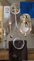 Overview of six teaspoons, dinner fork, pierced server, gravy boat, glass coaster and two candlesticks on table
