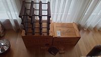 Full view of the wine rack, wooden wine box, one advertisement box, and glassware on a wooden floor near window curtains.