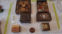 Overview of six decorative boxes made of wood and brass with carved, inlaid, and hand painted designs on a table