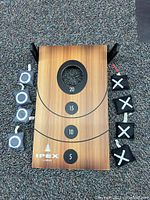 Top view of wooden bean bag throw game board with scoring rings (5, 10, 15, 20) and hole. Eight bean bags displayed around board: four marked with 'X' and four marked with 'O'.
