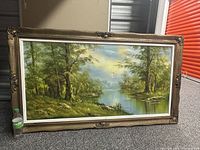 Framed oil painting resting against a storage unit door. Shows entire artwork and frame details.