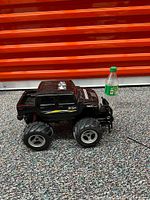 Black monster truck toy with large wheels and side decals, placed upright beside a green bottle