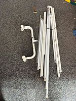Disassembled white metal clothing rack tubes and parts arranged on carpet