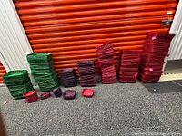 Photo showing stacks of colored gift baskets arranged by color (green, purple, red) and size, outside near orange storage unit doors.