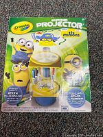 Box showing Crayola Sketcher Projector with Minions characters, claims up to 20x larger projection on walls or ceiling, includes 4 markers and 3 tracing discs.