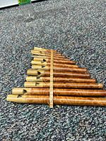 Close-up side view of 10 wooden pan flute pipes arranged by length on carpeted floor.