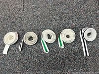 Five white karate belts, some with green and black stripes, laid out on carpeted floor for condition and color display.