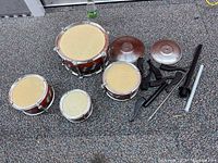 Photo showing four drums, two cymbals, multiple black stands, and a silver stand tube laid out on a grey carpeted floor
