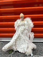 Photo of white fairy figurine against orange background, showing detailed lace dress and feathered wings, with attached light cords.
