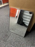 Mirror leaning against cardboard box and reflecting storage unit door and other items