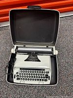 Front view of a white and black Remington typewriter inside a black carrying case, the top cover is open showing keyboard and carriage.