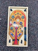 Top view of the wooden pinball game showing colorful playfield with bumpers, flippers, and spring launcher.