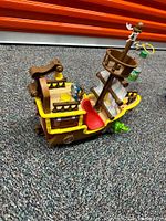 Side angle showing the detailed wooden elements, yellow railings, red captain's chair, and figure on the mast with a yellow steering wheel.