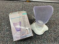 Photo of Steam Facial device on carpet with original box showing packaging and device features.