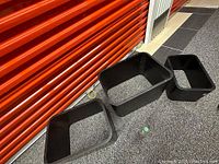 Photo of three black plastic rectangular planter boxes in varying sizes on a gravel floor in front of a red storage door, showing some scuff marks and wear.