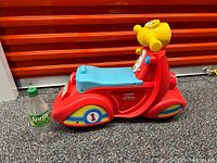 Side view of red plastic toddler ride-on scooter toy with blue seat and yellow handlebars next to a Sprite bottle for scale.