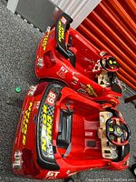 Two red 6V toddler ride-on toy cars placed side by side, showing left-side and top views with steering wheels and cockpit details